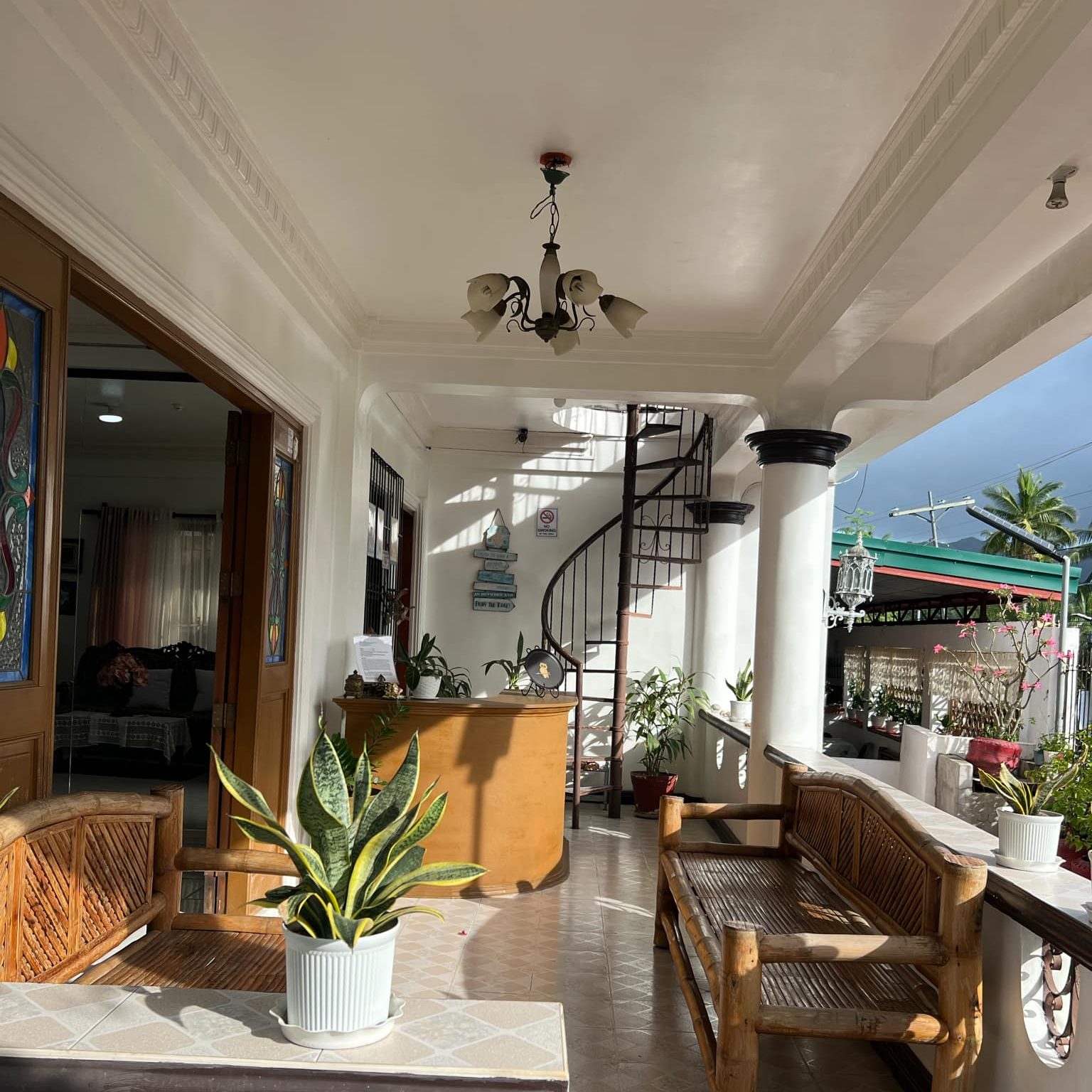 Veranda with bamboo chairs large entry doors on the left and spiral staircase in the back
